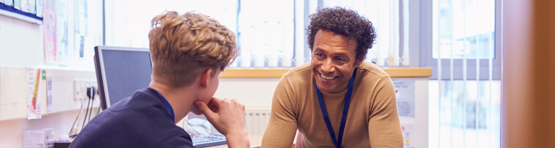 A smiling guidance counsellor sitting across from a male student both seem to be in discussion